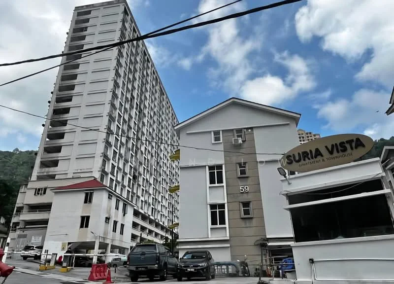 Exterior type: mid-rise condominium; features: white painted facade, grey accent wall, multiple-storey building, surrounded by greenery, parking area visible, signage for Suria Vista, cloudy sky, urban setting; style: modern.