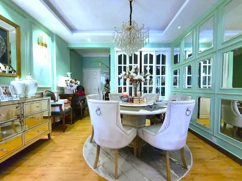 Dining features: round dining table, upholstered dining chairs, chandelier, mirrored sideboard, green painted walls, wood flooring, decorative wall mirrors, crown moulding, table centerpiece with flowers; style: luxury.