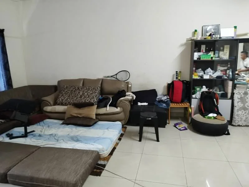 Living features: 3-seater fabric sofa in beige, 2-seater fabric sofa in brown, coffee table, area rug, tile flooring, white painted walls, black curtains, bookshelf with various items, floor cushions, decorative wall frame, cluttered with personal items.