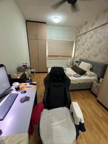 Bedroom features: queen-size bed with grey upholstered headboard, wooden flooring, light grey wallpaper with floral pattern, built-in wardrobe with sliding doors, desk with computer monitor, black gaming chair, window with blinds, ceiling light fixture, decorative bedside table, white bedding, area rug; style: modern.