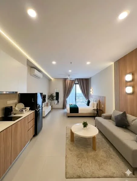 Living features: open-plan layout, grey fabric sofa, round coffee table with wooden legs, wall-mounted TV, light wood cabinetry, white countertop, stainless-steel fridge, built-in oven, microwave, recessed LED downlights, floor-to-ceiling window, curtains, bed with green bedding, decorative wall lights, light-colored flooring; style: modern; view: city.