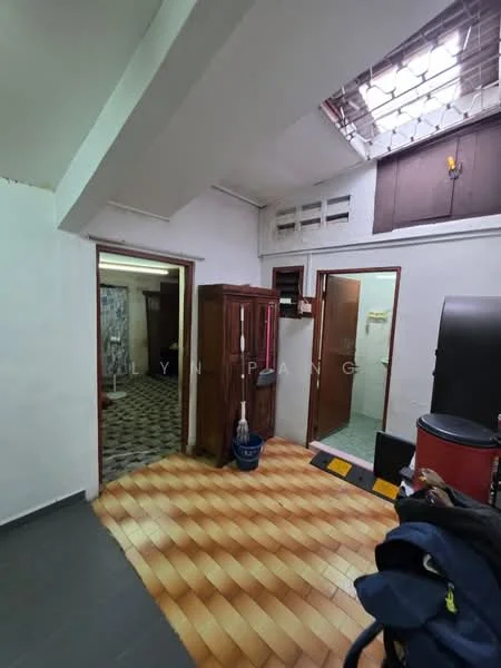 Room features: white painted walls, grey tiled flooring, wooden cabinet, door to bathroom, door to another room, skylight, ceiling light, wall-mounted hooks, black refrigerator, red storage container.