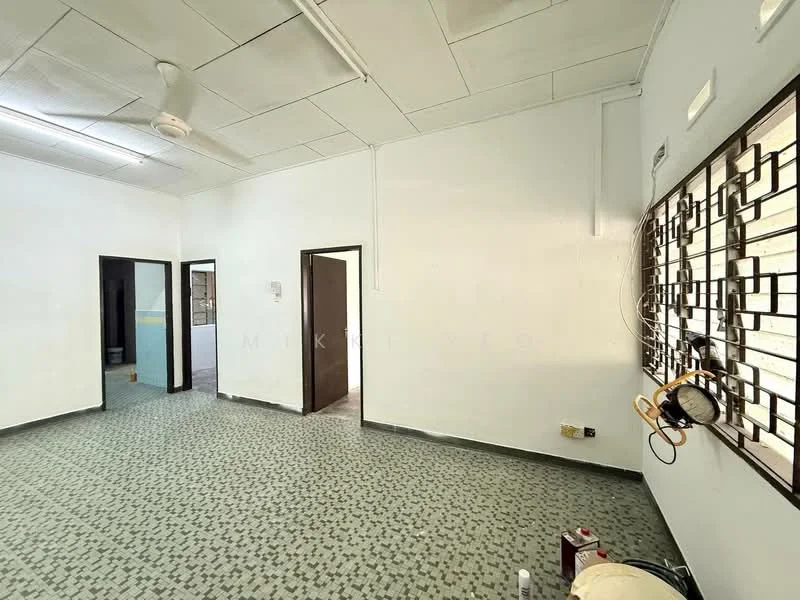 Room features: white painted walls, ceiling fan, green patterned flooring, two doorways, window with decorative grille, light fixture on ceiling, no visible furniture, plain ceiling.