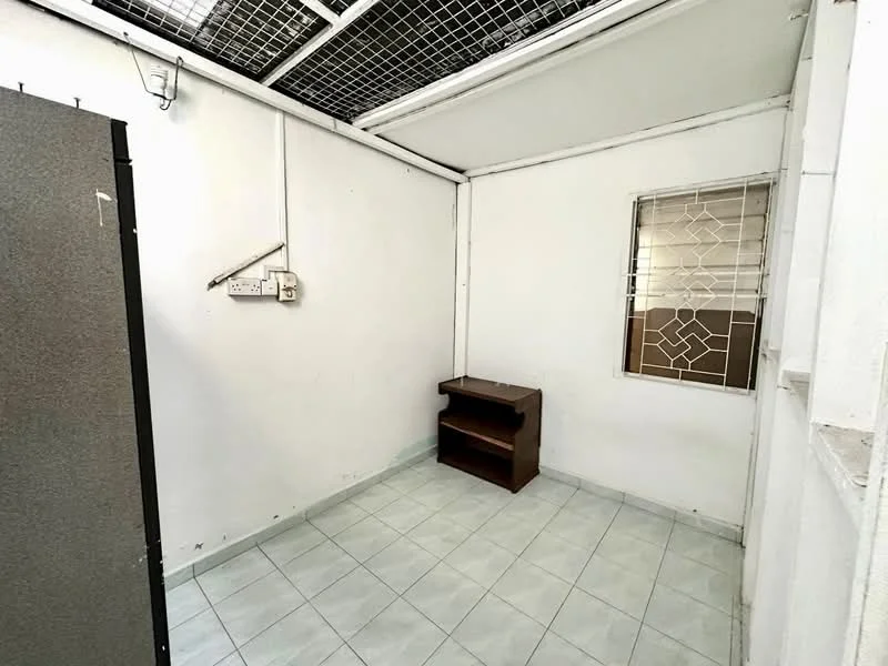 Room features: white painted walls, tile flooring, window with security grille, shelving unit, exposed ceiling, fluorescent light fixture, corner space, no visible appliances.