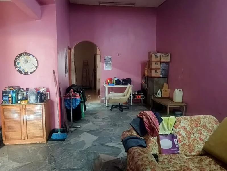 Room features: pink painted walls, grey stone flooring, wooden cabinet, various containers on cabinet, clothes rack with hanging clothes, office chair, boxes stacked against wall, sofa with floral pattern, broom, laundry items on floor.