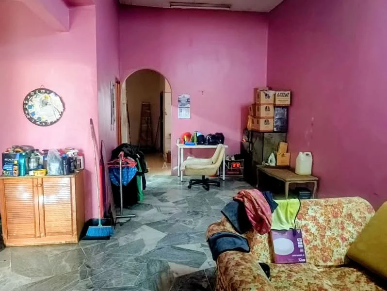 Room features: pink painted walls, marble flooring, wooden cabinet, cardboard boxes, plastic containers, office chair, folding clothes rack, sofa with floral pattern, mirror on wall, doorway leading to another room.