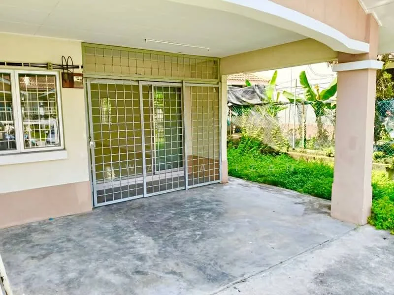 Exterior features: concrete flooring, metal security grille, large sliding glass door, surrounded by greenery, fenced area, exterior wall with cream paint, roof overhang; style: modern.