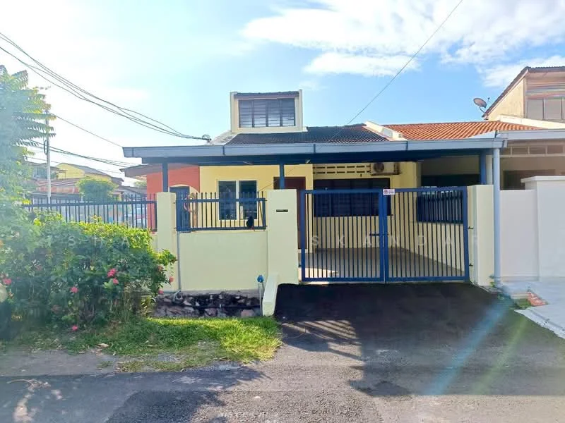 Exterior type: semi-detached house; features: yellow painted facade, flat roof, single-storey, manicured lawn, fenced front yard with gate, paved driveway, garden with flowering plants, front porch, visible windows, security grille on windows; style: modern.