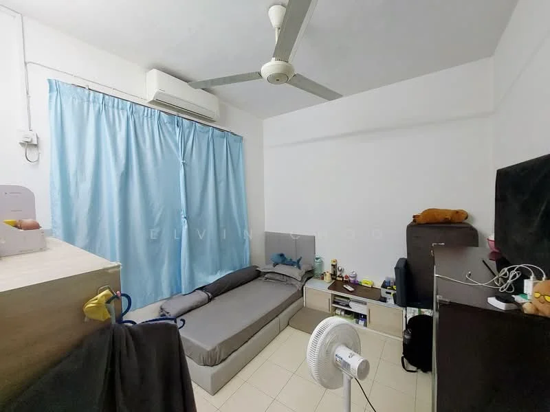 Bedroom features: light blue curtains, wall-mounted split AC, ceiling fan, single bed with grey bedding, wooden bedside table, dark wooden dresser, white walls, tile flooring, decorative items on dresser, fan on floor.