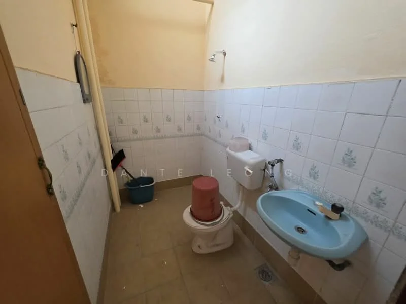 Bathroom features: white tiled walls with floral pattern, beige tiled flooring, one-piece toilet, sink with faucet, shower head, wall-mounted mirror, plastic waste bin.