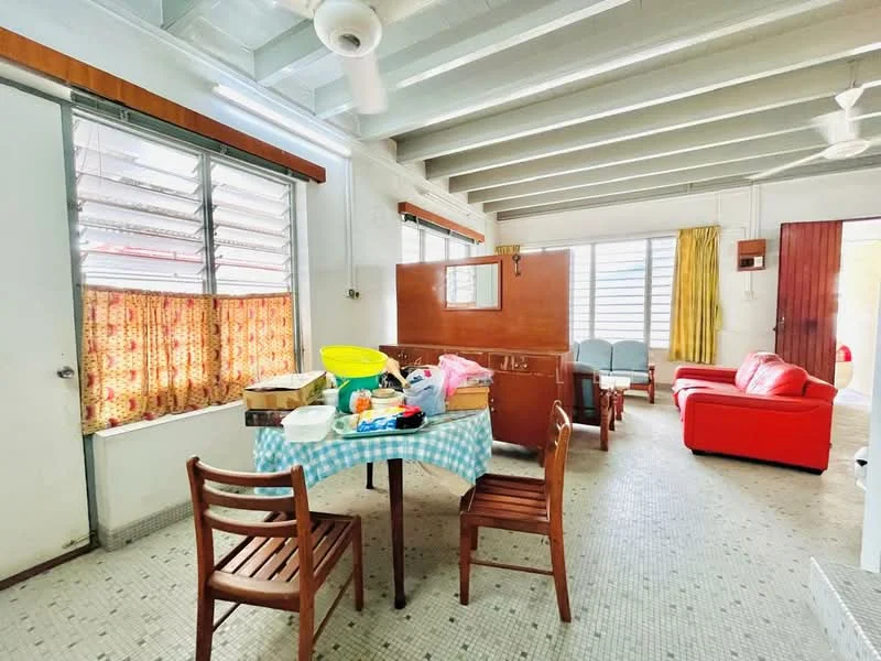 Living features: red leather sofa, wooden dining table with checkered tablecloth, 4 wooden dining chairs, ceiling fan, exposed beams, large windows with metal grilles, curtains with floral pattern, tiled flooring, wall-mounted light switch, open layout, decorative wall panel, door leading outside.