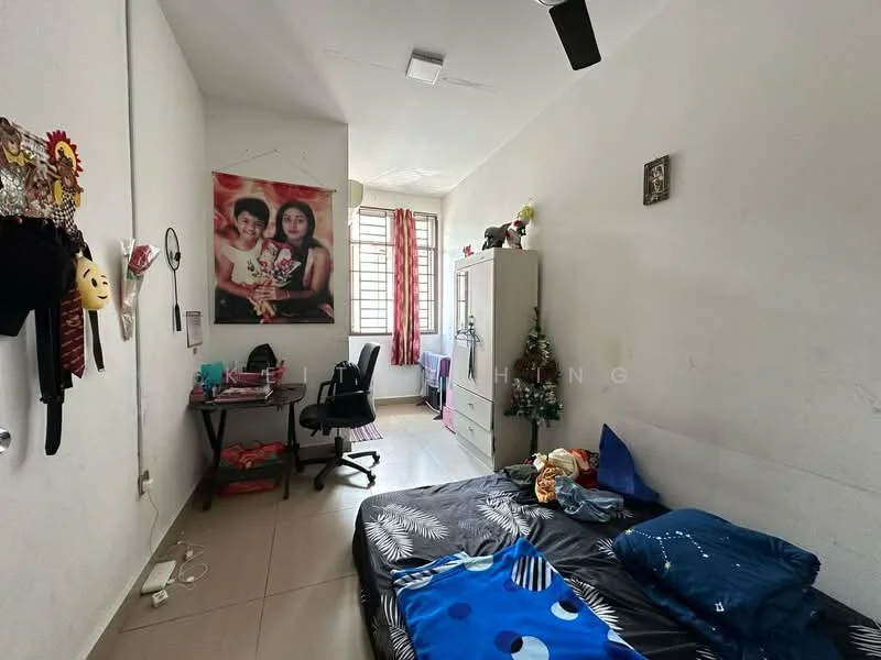 Bedroom features: white painted walls, tile flooring, single bed, black bedspread with floral pattern, blue decorative pillows, study desk with chair, wall-mounted shelf, window with red curtains, ceiling fan, framed artwork on wall, decorative wall hanging.