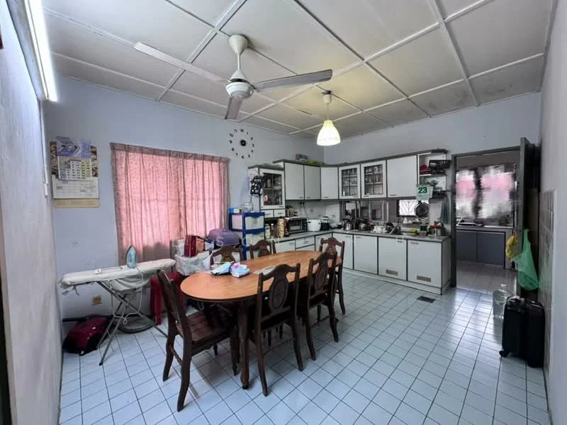 Kitchen features: white painted walls, tile flooring in light blue, ceiling with grid panels, 5-blade ceiling fan, pendant light, wooden dining table with 6 chairs, stainless-steel sink, built-in cabinets with glass doors, countertop with appliances, microwave, refrigerator, window with sheer curtains, ironing board, laundry basket, suitcase.