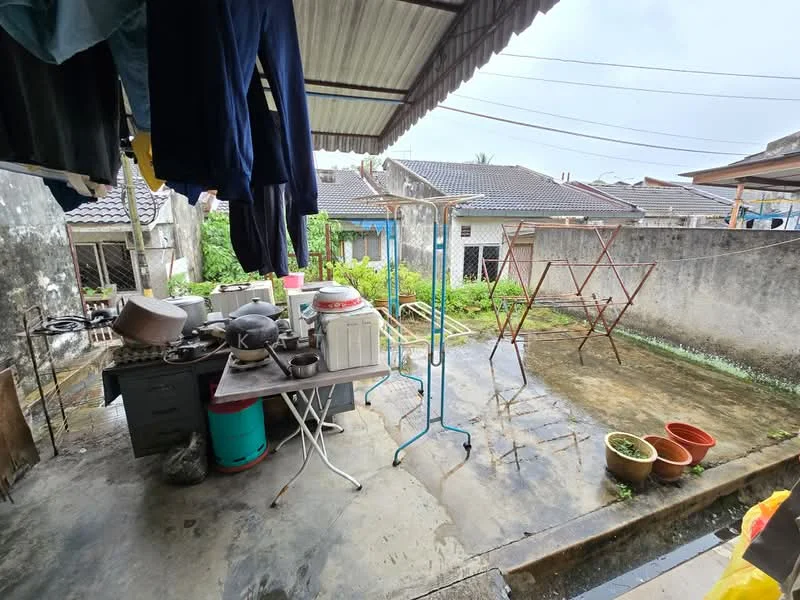 Room features: concrete flooring, metal roof with overhang, outdoor clothes drying rack, plastic storage containers, various pots with plants, outdoor sink, wooden table, metal folding chair, exposed brick wall, greenery visible in background; view: garden.