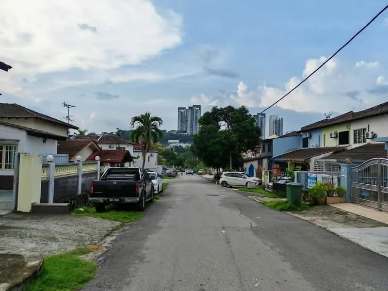 Exterior type: linked terrace house; features: residential street view, paved road, manicured lawns, mature trees, single-storey houses, multi-storey buildings in background, utility poles, visible vehicles parked on street; style: modern.