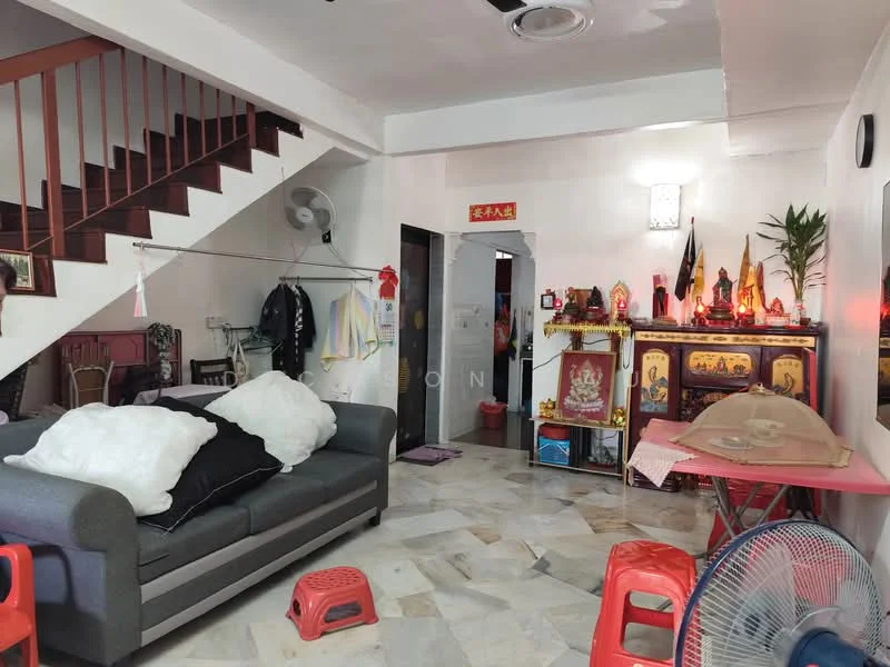 Living features: grey fabric sofa, white throw pillows, marble flooring, wall-mounted ceiling fan, decorative altar with offerings, red plastic stools, wooden staircase, wall-mounted light fixture, potted plant, clothes hanging on rack; style: traditional.