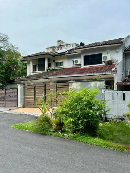 Exterior type: semi-detached house; features: two-storey structure, brown tiled roof, cream painted facade, wooden gate, manicured garden with shrubs, driveway with paving stones, visible air conditioning units, surrounded by greenery, fenced perimeter, windows with black grills; style: modern.