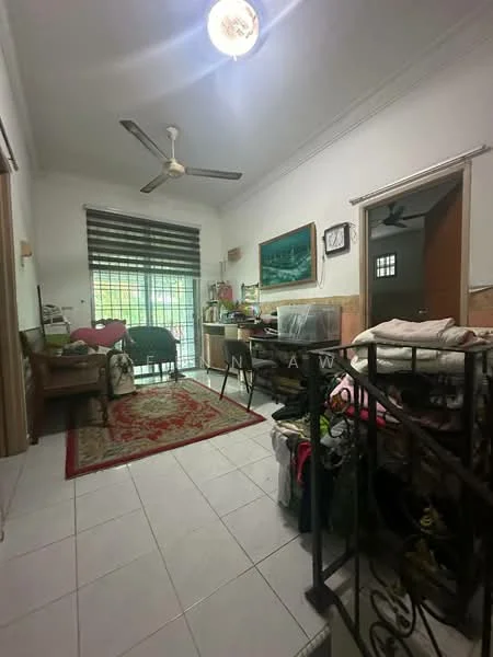 Room features: white painted walls, white tiled flooring, 5-blade ceiling fan, window with black horizontal blinds, green armchair, wooden table, decorative area rug with red pattern, shelves with various items, doorway leading to another room, decorative painting on wall, multiple storage items, indoor plants; style: traditional; view: garden.
