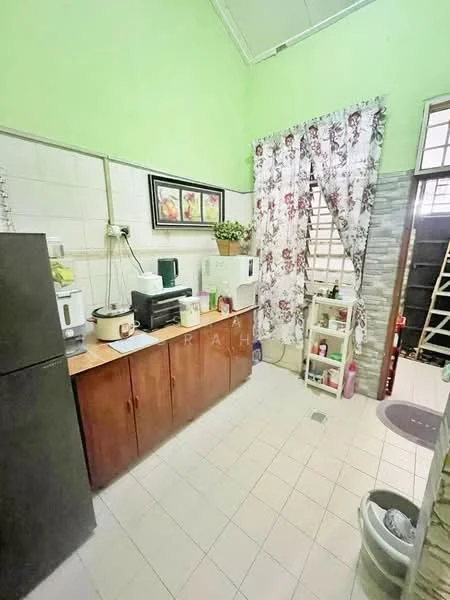 Kitchen features: green painted walls, white tiled backsplash, wooden cabinetry, black refrigerator, microwave, kettle, toaster, countertop with appliances, floor tiles, curtains with floral pattern, sink, open shelving, trash bin.