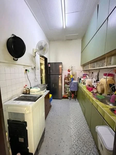 Kitchen features: green cabinetry, white tiled backsplash, stainless-steel fridge, washing machine, sink, countertop with yellow edge, ceramic tile flooring, wall-mounted fan, open shelving, various kitchen utensils and appliances.