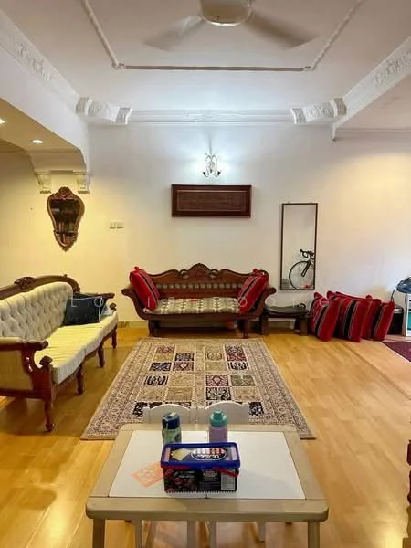 Living features: wooden flooring, white painted walls, crown moulding, 5-blade ceiling fan, sofa with upholstered cushions, wooden coffee table, decorative area rug, wall-mounted mirror, bookshelf, bicycle, red decorative cushions; style: traditional.