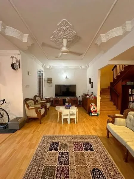 Living features: wooden flooring, white painted walls, tray ceiling with decorative moulding, 5-blade ceiling fan, wall-mounted TV, sofa set with upholstery, coffee table, area rug with intricate pattern, decorative wall clock, bicycle, children's toy, staircase leading to upper floor; style: traditional.