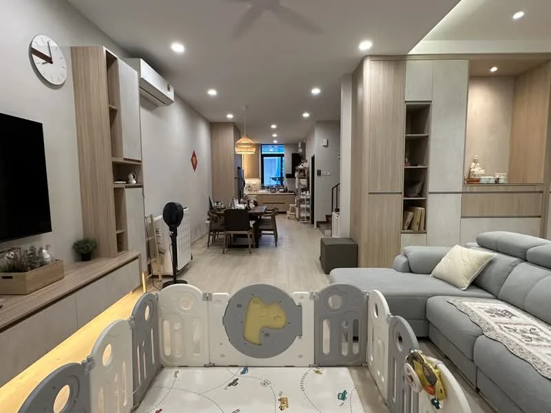 Living features: light wood flooring, white painted walls, ceiling fan, wall-mounted TV, TV console with storage, sofa in light grey, decorative wall clock, recessed downlights, large window with natural light, open layout to dining area, children's playpen, dining table with chairs visible in background; style: modern.