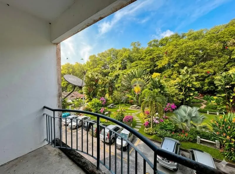 Balcony features: metal railing, concrete flooring, view of landscaped garden, view of parked cars, surrounded by greenery, sunny weather, blue sky, tropical plants; view: garden.