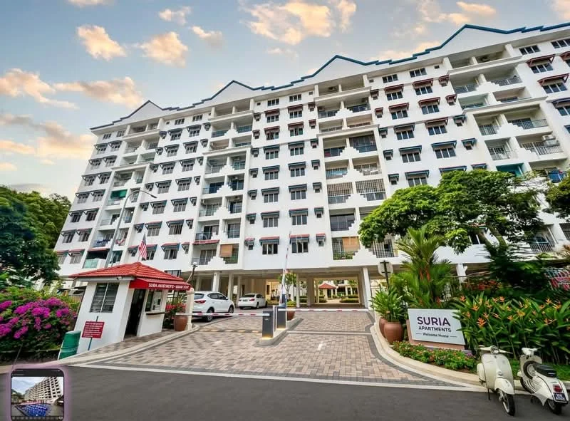 Exterior type: low-rise apartment block; features: white painted facade, recessed balconies, flat roof, approximately 5-storey, manicured landscaping, paved driveway, guard house at entrance, parking spaces visible, tropical landscaping with palm trees, flowering plants in garden beds; style: modern.