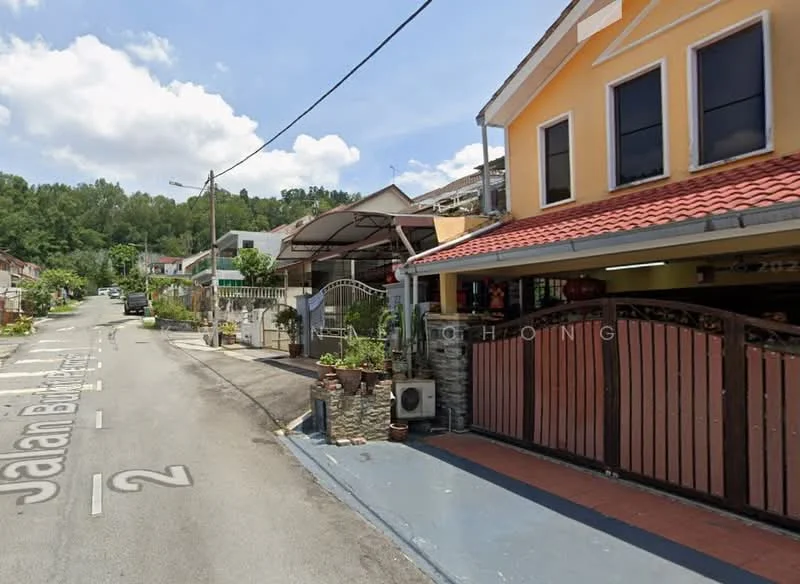 Exterior type: semi-detached house; features: yellow painted facade, red tiled roof, front porch with awning, brick wall fencing, landscaped garden with plants, air conditioning unit visible, paved driveway, street view with residential houses, surrounded by greenery; style: modern.