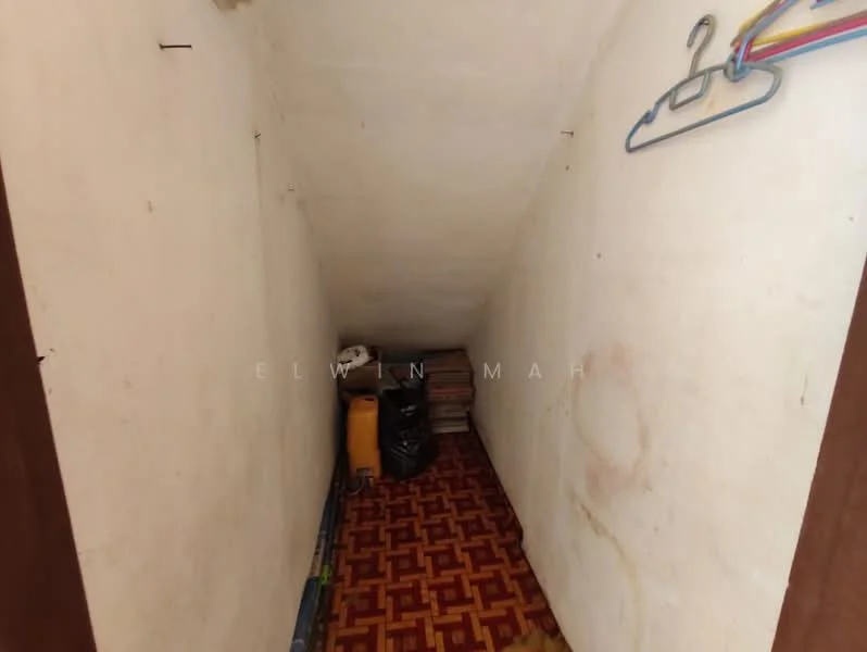 Room features: sloped ceiling, white painted walls, brown wooden door, brown patterned flooring, storage boxes, hanging clothes, visible clutter.
