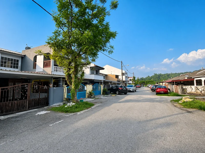 Exterior type: linked terrace house; features: two-storey linked terrace houses, driveway with interlocking pavers, manicured trees along the street, street lighting, open parking spaces, surrounded by residential area, clear blue sky, mountain view in background; style: modern.