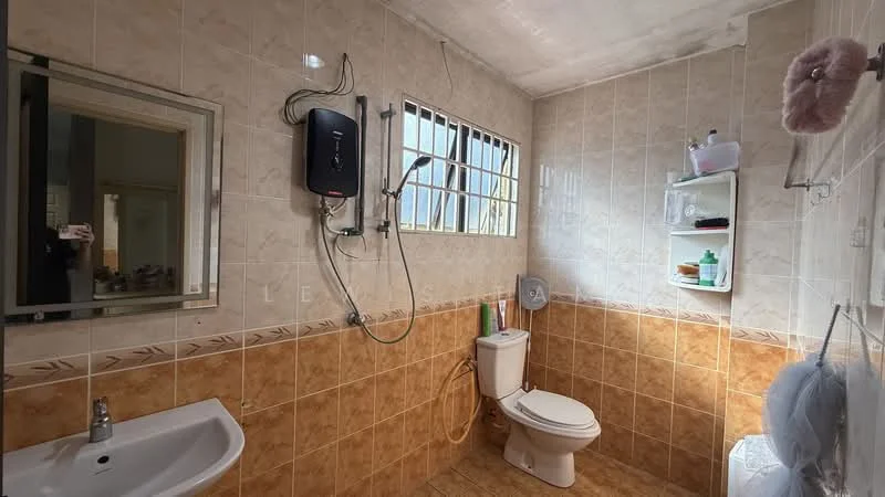 Bathroom features: white ceramic sink, chrome basin mixer faucet, one-piece toilet, shower with handheld shower head, wall-mounted water heater, tile cladding on walls, brown ceramic tile flooring, mirror with frame, open shelving for toiletries, window with metal bars.