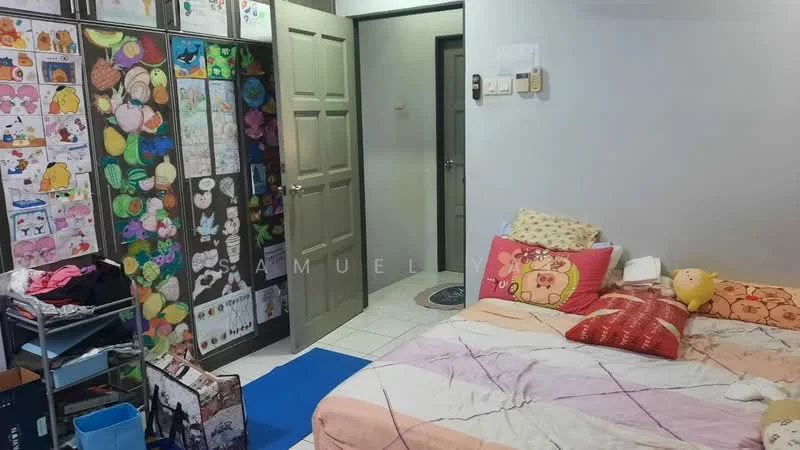 Bedroom features: queen-size bed with colorful bedding, decorative pillows, wooden wardrobe with colorful stickers, artwork on walls, tile flooring, white painted walls, door leading to hallway, blue area rug, storage cart with multiple drawers, clothes on the floor.