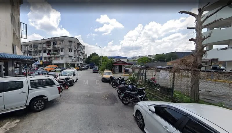 Exterior type: low-rise apartment block; features: multiple parked cars, fenced area, surrounding greenery, two-storey building, balconies visible on building, street view, cloudy sky, paved road; style: modern.