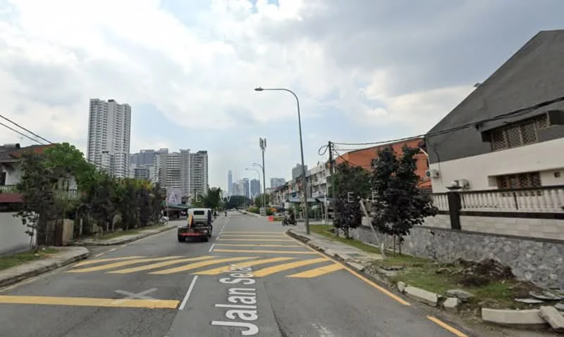 Exterior features: residential street, two-way road, yellow road markings, sidewalks, streetlights, trees along the road, high-rise buildings in the background, low-rise buildings on the side, cloudy sky; style: modern.