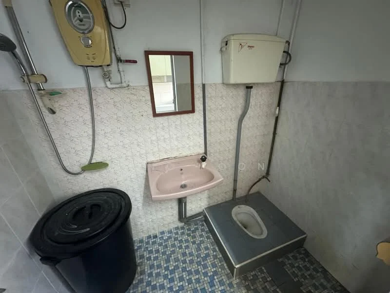 Bathroom features: pink sink, wall-mounted mirror, toilet squat, shower with wall-mounted water heater, grey tiled flooring, white tiled walls, waste bin.