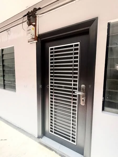 Exterior features: metal security door with horizontal slats, grey painted facade, glass windows with black frames, electric meter box mounted on wall, concrete flooring, simple architectural design; style: modern.