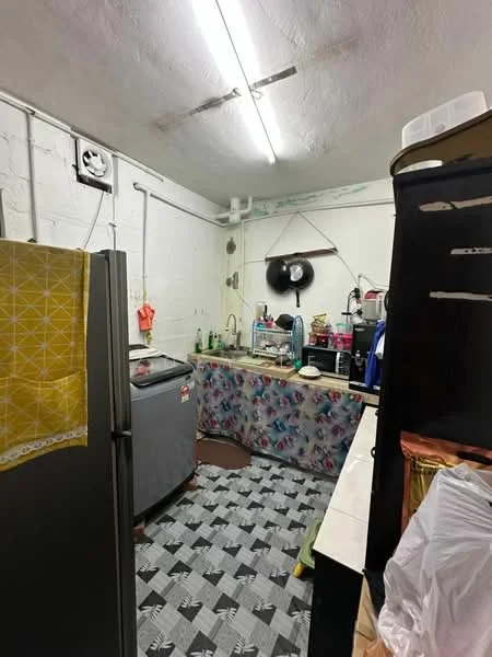 Kitchen features: grey tiled flooring, white painted walls, fluorescent ceiling lights, stainless-steel fridge, chest freezer, single-bowl sink, chrome faucet, countertop with storage underneath, kitchen utensils on countertop, wall-mounted clock, open shelving, decorative tablecloth.