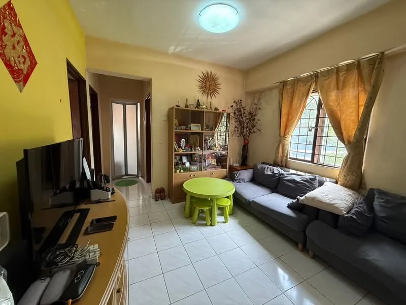 Living features: yellow painted walls, white tiled flooring, sofa in grey, green round coffee table, TV console, wall-mounted TV, curtains in beige, decorative wall clock, shelves with decorative items, floor-to-ceiling window, natural light from window.
