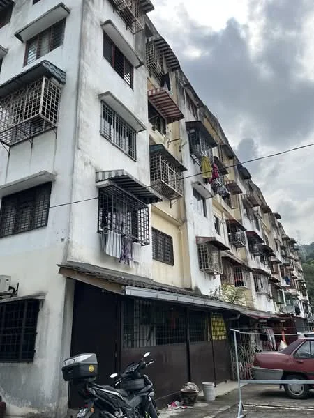 Exterior type: low-rise apartment block; features: white painted facade, grilled windows, balconies with laundry hanging, multiple storeys, exposed concrete, air conditioning units visible, parking area in front, surrounded by greenery; style: traditional.
