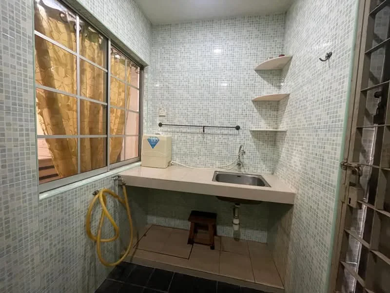 Laundry features: green mosaic tile walls, grey countertop, single-bowl stainless-steel sink, wall-mounted faucet, open shelving, stool, floor tiles in dark colour, window with sheer curtains.