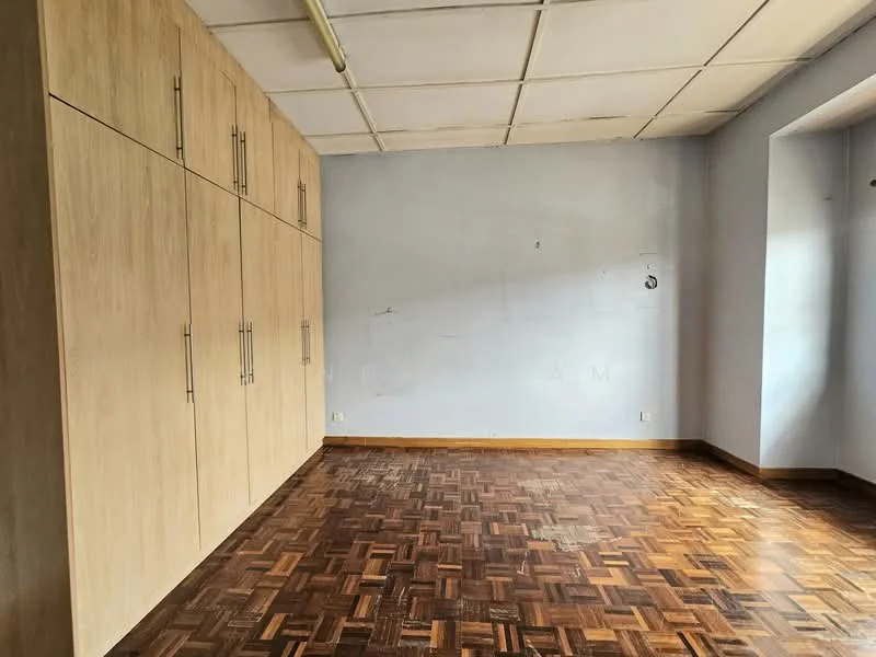 Room features: wooden parquet flooring, light grey painted walls, built-in cabinetry with wooden finish, ceiling with visible grid tiles, window with natural light.