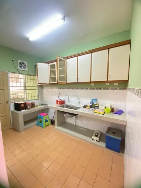 Kitchen features: green painted walls, white upper cabinets with glass doors, grey countertop, single-bowl stainless-steel sink, chrome pull-down faucet, built-in kitchen cabinet, tile backsplash, ceramic tile flooring, window with grid pattern, overhead fluorescent lighting, stool in blue, various kitchen appliances and utensils on countertop.