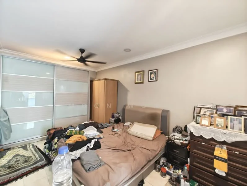 Bedroom features: queen-size bed with beige bedding, upholstered headboard, wooden wardrobe with sliding doors, wooden dresser with multiple framed photos, ceiling fan, cream painted walls, tile flooring, decorative wall art, area rug, cluttered with clothes and personal items.