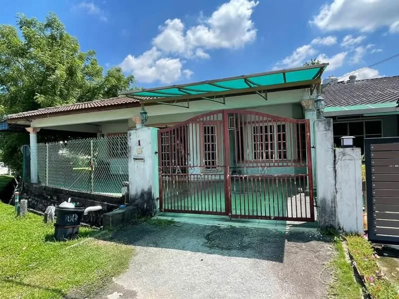 Exterior type: detached bungalow; features: single-storey, red metal gate, green awning over porch, white painted facade, gravel driveway, manicured lawn, fence with green mesh, front porch area, mature trees in vicinity, clear blue sky; style: traditional.