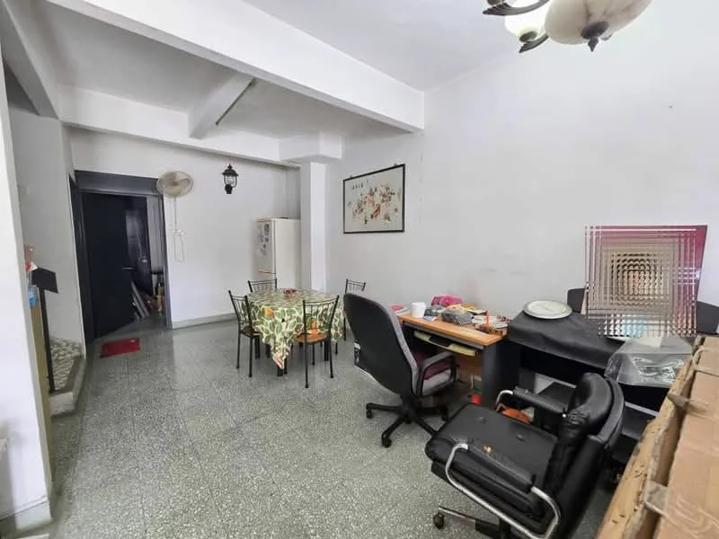 Dining features: dining table with floral tablecloth, black dining chairs, green speckled flooring, white walls, ceiling light fixture, wall-mounted artwork, computer desk with chair, office chair, refrigerator, open layout to adjacent room. Room features: doorway leading to another room, wall-mounted fan.