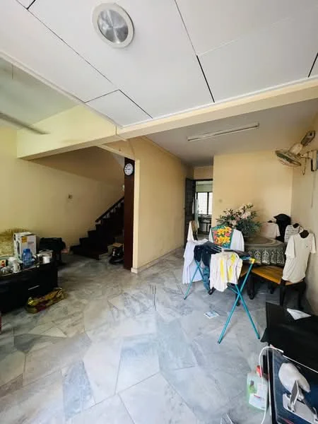 Room features: marble flooring, cream painted walls, staircase with wooden railing, wall-mounted air conditioning unit, clock on wall, clothes drying rack, black storage cabinet, various items on floor, decorative plant on table, folding chairs, clothes hanging on furniture.