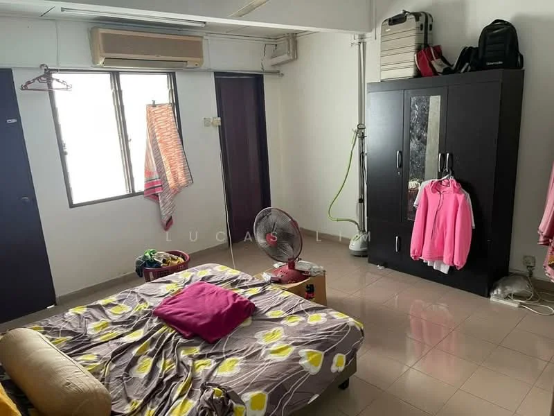 Bedroom features: queen-size bed with floral bedding, wooden wardrobe with mirrored doors, wall-mounted air conditioning unit, floor fan, light-colored tiled flooring, white painted walls, curtains on windows, clothes hanging on hooks.