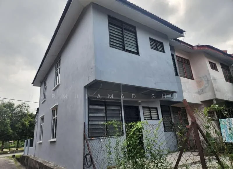 Exterior type: semi-detached house; features: light blue painted facade, two-storey structure, sloped red tile roof, multiple windows with grilles, fenced yard with overgrown grass, concrete pathway, surrounded by greenery; style: modern.